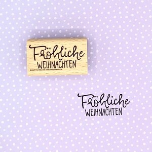 Peut inclure: Un tampon en bois avec le texte "Fr&ouml;hliche Weihnachten" en encre noire.