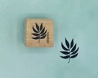Peut inclure: Un tampon en bois avec une silhouette noire d'une feuille. Le tampon est rectangulaire et de couleur brun clair.
