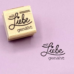 May include: Wooden stamp with the text "mit Liebe gen&auml;ht" which translates to "with love sewn" in English. The stamp has a small heart symbol above the word "Liebe".