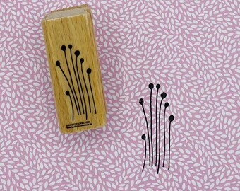 May include: A wooden rubber stamp with a design of a cluster of tall, thin stems with small circles at the top. The stamp is on a pink background with a white pattern.