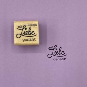May include: Wooden stamp with the text "mit Liebe gen&auml;ht" which translates to "with love sewn" in English. The stamp is on a purple background.