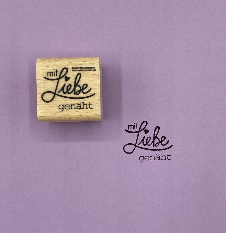 May include: Wooden stamp with the text "mit Liebe gen&auml;ht" which translates to "with love sewn" in English. The stamp is on a purple background.