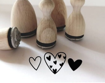Peut inclure: Quatre tampons en bois avec différents motifs de cœurs. Les tampons sont en bois naturel et ont un tampon d'encre noir. Les motifs comprennent un cœur simple, un cœur avec un motif de petits cœurs et un cœur noir uni.