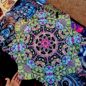 May include: A brightly coloured garment featuring a psychedelic pattern in neon green, blue, pink, and black. The central design is a kaleidoscope. Other items with similar patterns are visible. The garment is being held by a hand.