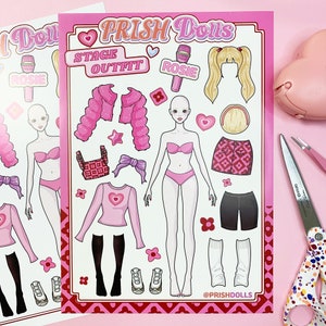 May include: A pink and white paper doll set with the words "PRISH Dolls" and "Stage Outfit" at the top. The set includes a doll, a microphone, a pink puffy jacket, a pink top, a pink skirt, a pair of black shorts, a pair of white socks, and a pair of white shoes.