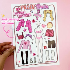 May include: A pink and white paper doll set with the text "PRISH Dolls" and "STAGE OUTFIT" in pink. The set includes a doll, clothing, accessories, and a microphone labelled "ROSIE".