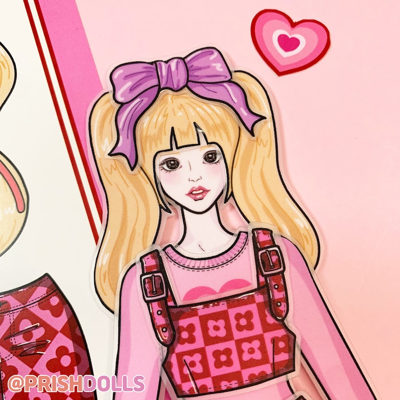May include: A paper doll with blonde hair, wearing a pink sweater and a red and pink checked overall dress. The doll has a purple bow in her hair and is holding a heart.