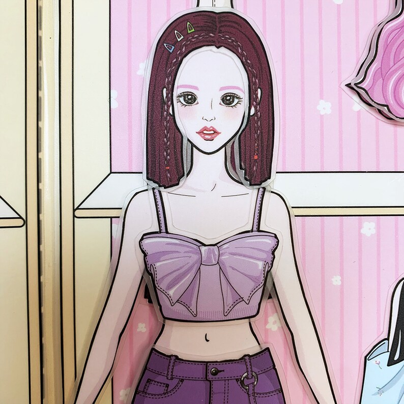 May include: A paper doll with long brown hair, wearing a purple crop top with a large bow and purple jeans. The doll is part of a larger set of paper dolls.