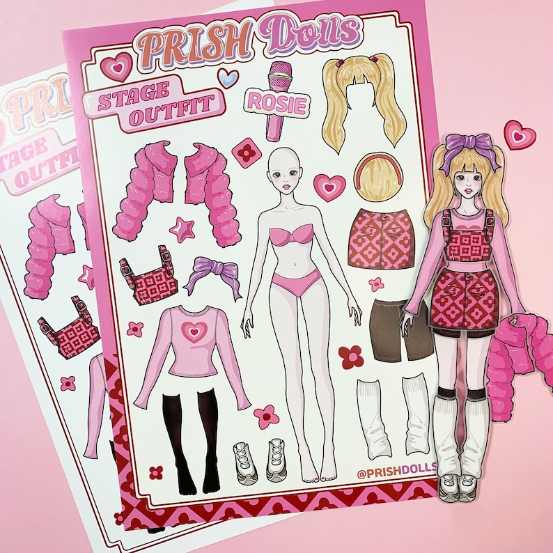 May include: A pink and white paper doll set with the words "PRISH Dolls" and "Stage Outfit" at the top. The set includes a doll, clothing, and accessories. The doll has pink hair and a pink dress. The clothing includes a pink jacket, a pink skirt, and a pink top. The accessories include a microphone, a heart, and a star.