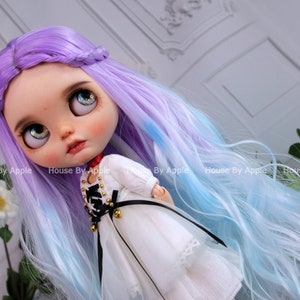 May include: A doll with long, wavy, purple and blue hair, wearing a white dress with black lace and gold accents.