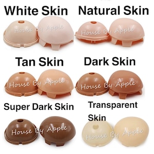 Puede incluir: Colección de cabezas de muñecas en varios tonos de piel: blanco, natural, bronceado, oscuro, súper oscuro y transparente. Cada cabeza tiene forma de cúpula con una base y el texto "House By Apple".