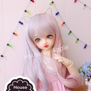May include: A doll with long, wavy, two-toned hair. The hair is light blue on one side and pink on the other. The doll is wearing a pink dress with white lace trim and a pearl headband with cat ears.