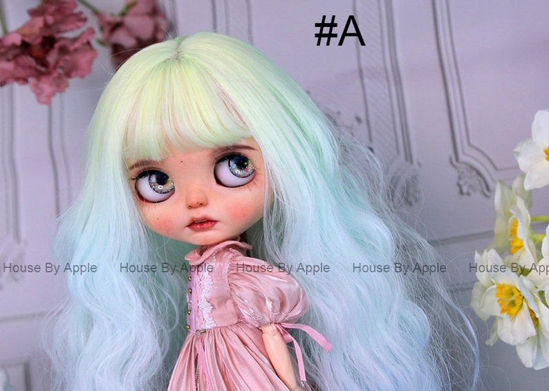 May include: A doll with long, wavy, light green and blue hair, wearing a pink dress with lace details. The doll has large, blue eyes with glitter.