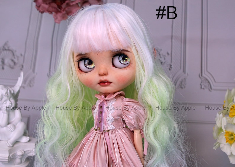 May include: A doll with long, wavy, green and white hair, wearing a pink dress with white lace trim. The doll has large, blue eyes with glitter accents. The doll is looking to the right of the image.