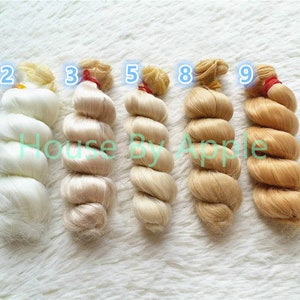 Peut inclure: Six m&egrave;ches de cheveux de poup&eacute;e dans diff&eacute;rentes nuances de blond, du blanc au brun clair, avec les num&eacute;ros 2, 3, 5, 8 et 9 &eacute;tiquet&eacute;s sur chaque m&egrave;che.