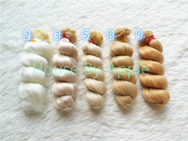 Peut inclure: Six m&egrave;ches de cheveux de poup&eacute;e dans diff&eacute;rentes nuances de blond, du blanc au brun clair, avec les num&eacute;ros 2, 3, 5, 8 et 9 &eacute;tiquet&eacute;s sur chaque m&egrave;che.