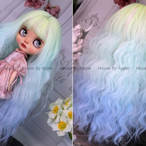 May include: A long, wavy doll wig with a light green to blue ombre color gradient. The wig is styled with bangs and has a natural, flowing texture.