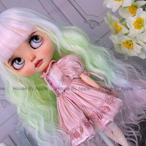 May include: A doll with long, wavy, green and pink hair, wearing a pink dress with lace trim. The doll has large, blue eyes and a painted face.