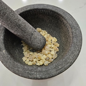 May include: A gray stone mortar and pestle with a pile of light yellow resin inside.