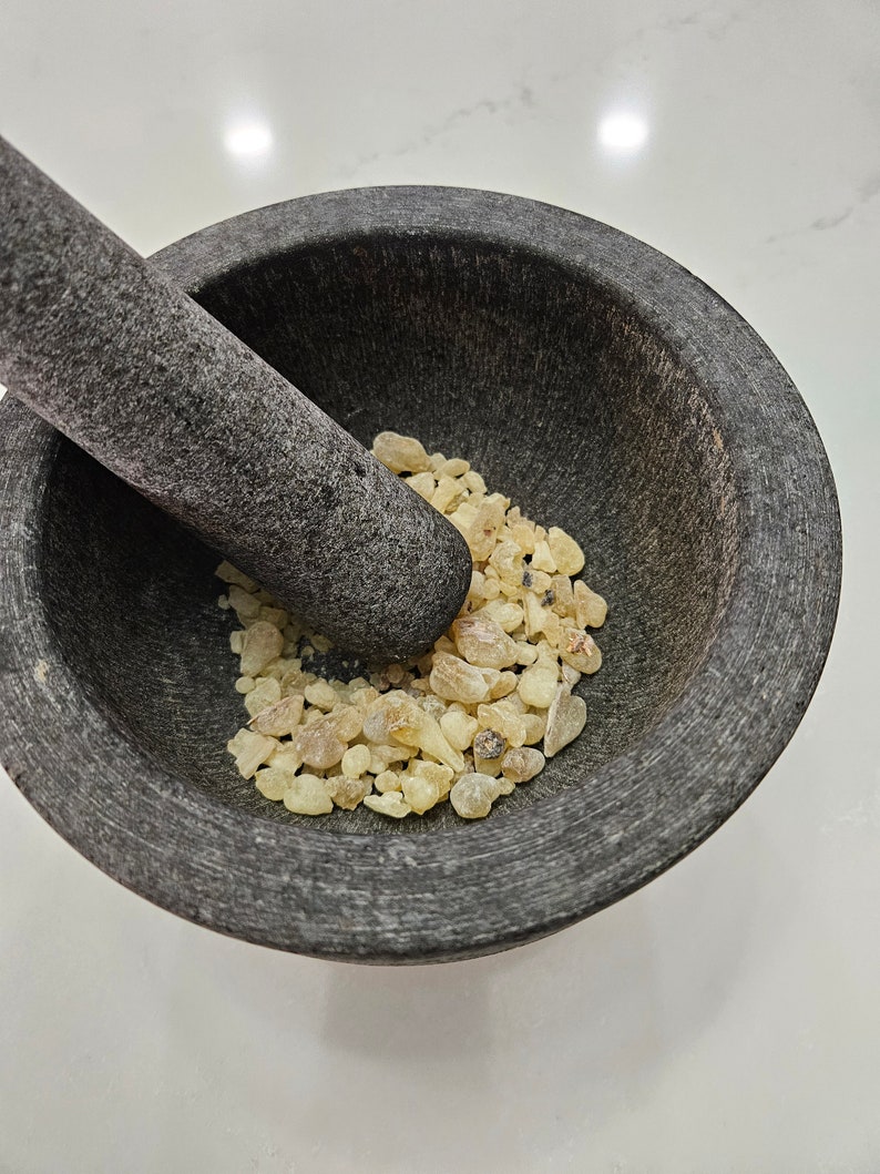 May include: A gray stone mortar and pestle with a pile of light yellow resin inside.