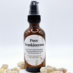 Puede incluir: Una botella de vidrio marrón con un dispensador de bomba negro. La etiqueta dice "Pure Frankincense" y enumera los ingredientes. La botella está rodeada de pequeños trozos de resina de color claro. El producto es de "Pure Nourish Skincare".