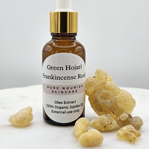May include: A brown glass bottle with a gold lid and dropper, labeled "Green Hojari Frankincense Resin Pure Nourish Skincare Oleo Extract 100% Organic Jojoba Oil External use only". The bottle is surrounded by small, yellow, resin pieces.