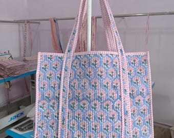 May include: A quilted tote bag with pink and blue floral print. The bag has pink and white striped straps.