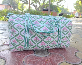 May include: A white and green floral print duffel bag with a green and white striped trim. The bag has two handles and a zipper closure.