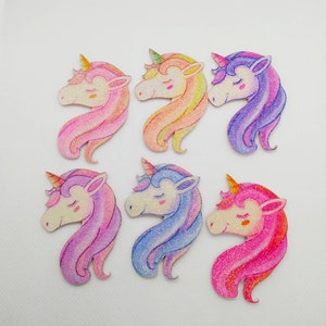 Peut inclure: Six découpes de tête de licorne en bois avec des accents de paillettes. Les licornes sont de différentes couleurs, notamment rose, violet et bleu.