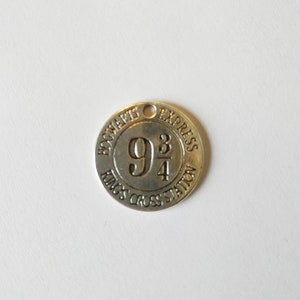 Peut inclure: Breloque en argent avec les mots "Hogwarts Express" et "King's Cross Station" entourant le numéro "9 3/4".