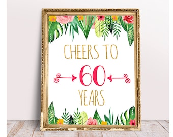 May include: A framed print with a gold border, featuring the text "CHEERS TO 60 YEARS" in gold glitter lettering. The number 60 is in pink with arrows. The frame is decorated with watercolor floral and tropical leaf accents.