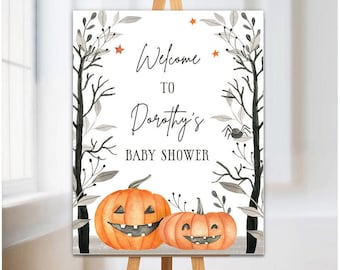 May include: A Halloween-themed baby shower sign on an easel. The sign features two orange jack-o'-lanterns and the text "Welcome to Dorothy's Baby Shower." The sign is framed with black branches, gray leaves, and orange stars.