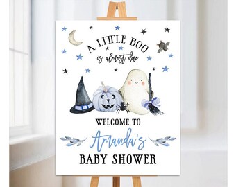May include: A white sign with blue accents announcing a baby shower. The sign says "A Little Boo is almost due" and "Welcome to Amanda's Baby Shower". The sign is decorated with a ghost, a witch's hat, a pumpkin, and stars.