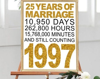 May include: A framed sign on an easel celebrating a 25th wedding anniversary. The sign has gold glitter text that reads "25 YEARS OF MARRIAGE" and includes the number of days, hours, and minutes. The year "1997" is also in gold glitter.