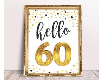 Può includere: Un cartello dorato glitter 'hello 60' con cuori neri e coriandoli dorati su uno sfondo bianco. Il cartello è incorniciato da una cornice dorata.