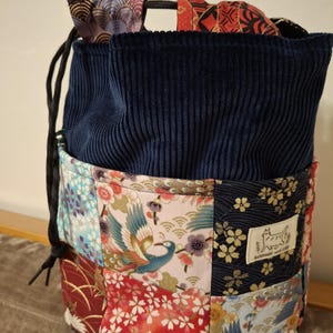 May include: A drawstring bag with a patchwork design. The top is navy blue corduroy, and the lower section features a patchwork of patterned fabrics with floral and bird motifs. The bag has a black drawstring closure.