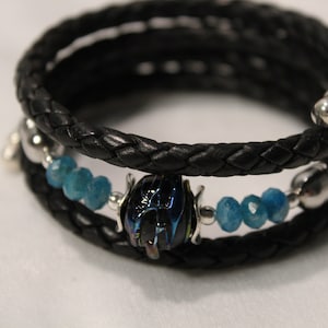 May include: A black leather wrap bracelet with blue gemstone beads and a silver beetle charm.