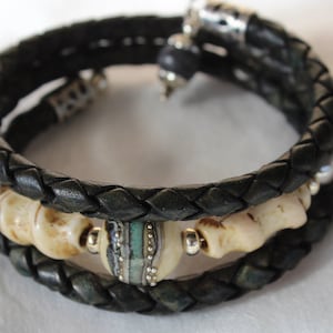 May include: A black leather bracelet with a braided design and white and blue beads. The bracelet has a silver clasp.