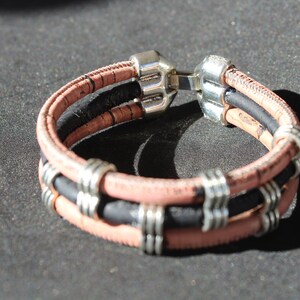 May include: A layered bracelet with black and pink cork and silver accents. The bracelet has a silver clasp.