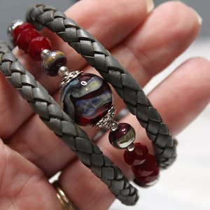 May include: A gray braided leather bracelet with red and clear glass beads and a large, multi-colored glass bead.