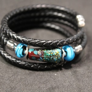 May include: A black leather wrap bracelet with three silver beads and a colorful glass bead in the center.