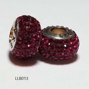 May include: Two silver charm beads with a red crystal design. The beads are round and have a hole in the center for threading onto a bracelet or necklace. The beads are marked with the text "925" and "LLB013".