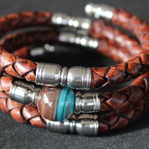 May include: A braided leather bracelet with silver metal accents and a brown and turquoise glass bead.