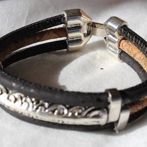 May include: A black leather bracelet with a silver metal clasp and a decorative silver metal band. The bracelet has a cork inlay.