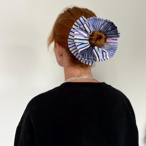 May include: A person with red hair wearing a black shirt and a colourful striped fabric scrunchie in their hair.