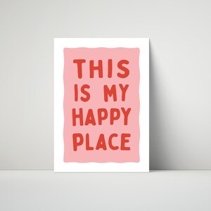 Pu&ograve; includere: Una stampa rettangolare bianca con la scritta "THIS IS MY HAPPY PLACE" in lettere rosse su sfondo rosa. La stampa &egrave; appoggiata a un muro bianco.