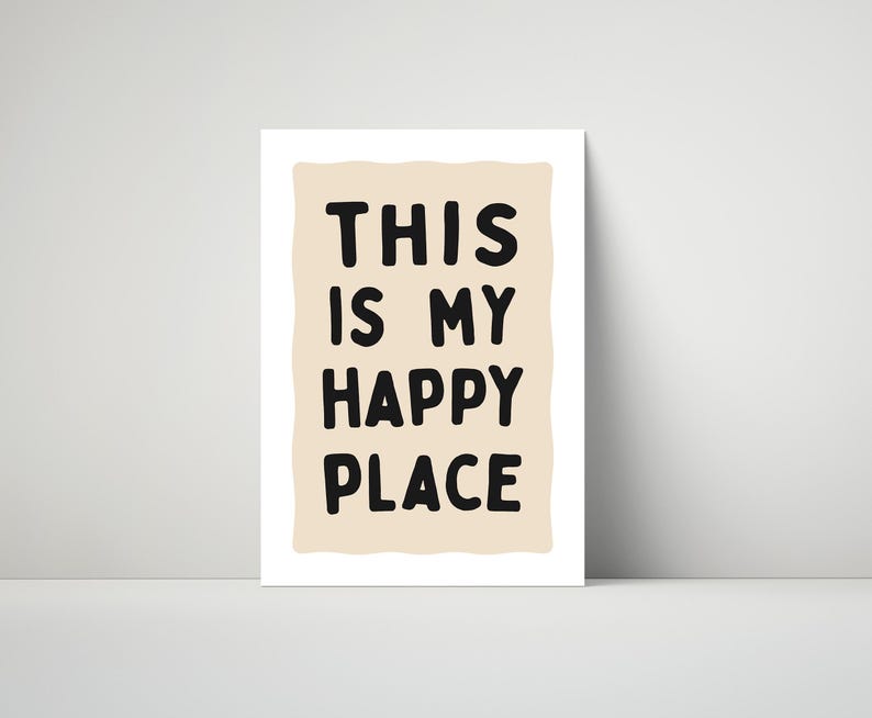 Pu&ograve; includere: Stampa incorniciata con la scritta "THIS IS MY HAPPY PLACE" in grassetto nero. Il testo &egrave; posto su uno sfondo beige chiaro di forma irregolare, con un bordo bianco. La stampa &egrave; esposta su una superficie bianca.