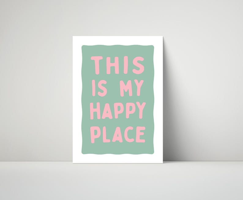 Pu&ograve; includere: Una stampa incorniciata con la scritta "THIS IS MY HAPPY PLACE" in lettere rosa su sfondo verde chiaro. La stampa ha un bordo bianco ed &egrave; esposta contro un muro bianco.