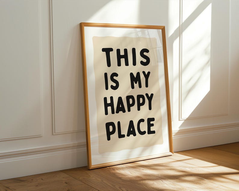 Pu&ograve; includere: Una stampa incorniciata con le parole "THIS IS MY HAPPY PLACE" in grassetto nero. La stampa ha uno sfondo beige e una cornice in legno marrone chiaro. &Egrave; appoggiata a un muro bianco e a un pavimento in legno.