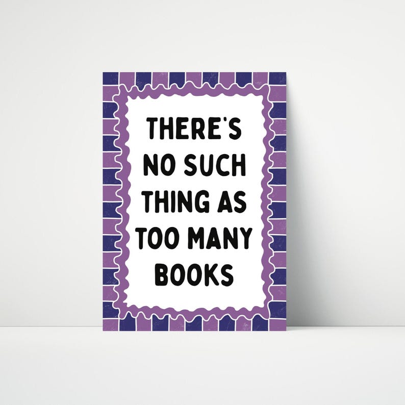May include: A rectangular sign with the text "THERE'S NO SUCH THING AS TOO MANY BOOKS" in black. The sign has a white background with a purple and blue decorative border.